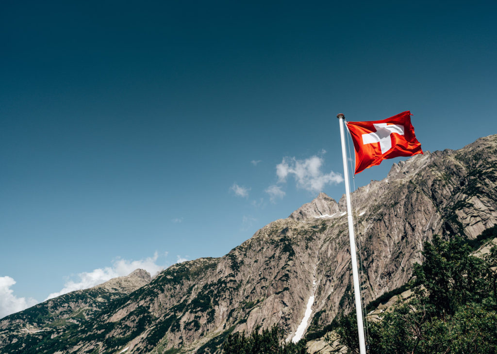 Swiss flag on a flagpole with mountains behind and a blue sky, to represent CH-REP deadline